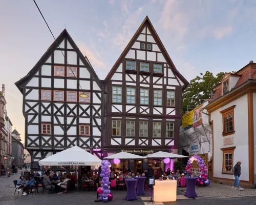 Fachwerkhäuser und eine Café-Terrasse mit violetten Luftballons in der Abenddämmerung.