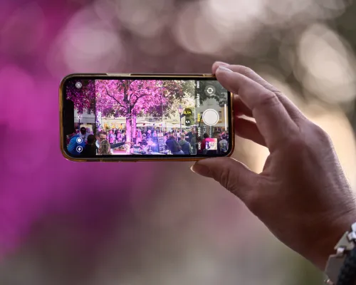 Eine Hand hält ein Smartphone waagerecht und fotografiert die violett beleuchtete Veranstaltung.