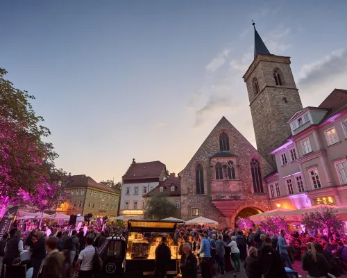 Kirche, Veranstaltungsgäste und ein Kaffeewagen auf dem Platz in der Abenddämmerung.