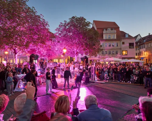 Tanzende führen vor einem Kreis von Zuschauenden auf dem violett beleuchteten Platz eine Choreografie auf.