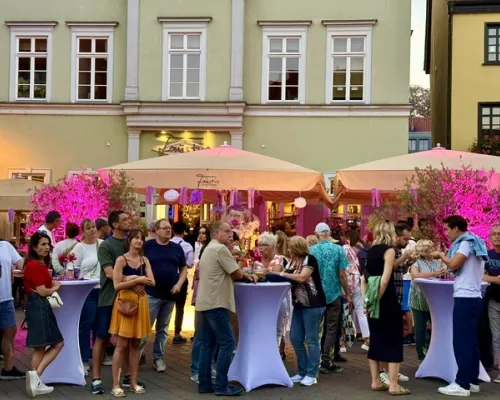 Abendliche Esstival-Szene mit Gästen, Stehtischen und violetter Beleuchtung
